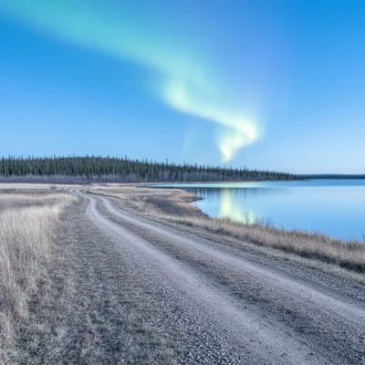 Wide prairie landscape in Manitoba at winter, with distant forest, a reflective lake, and faint aurora lights across the night sky.